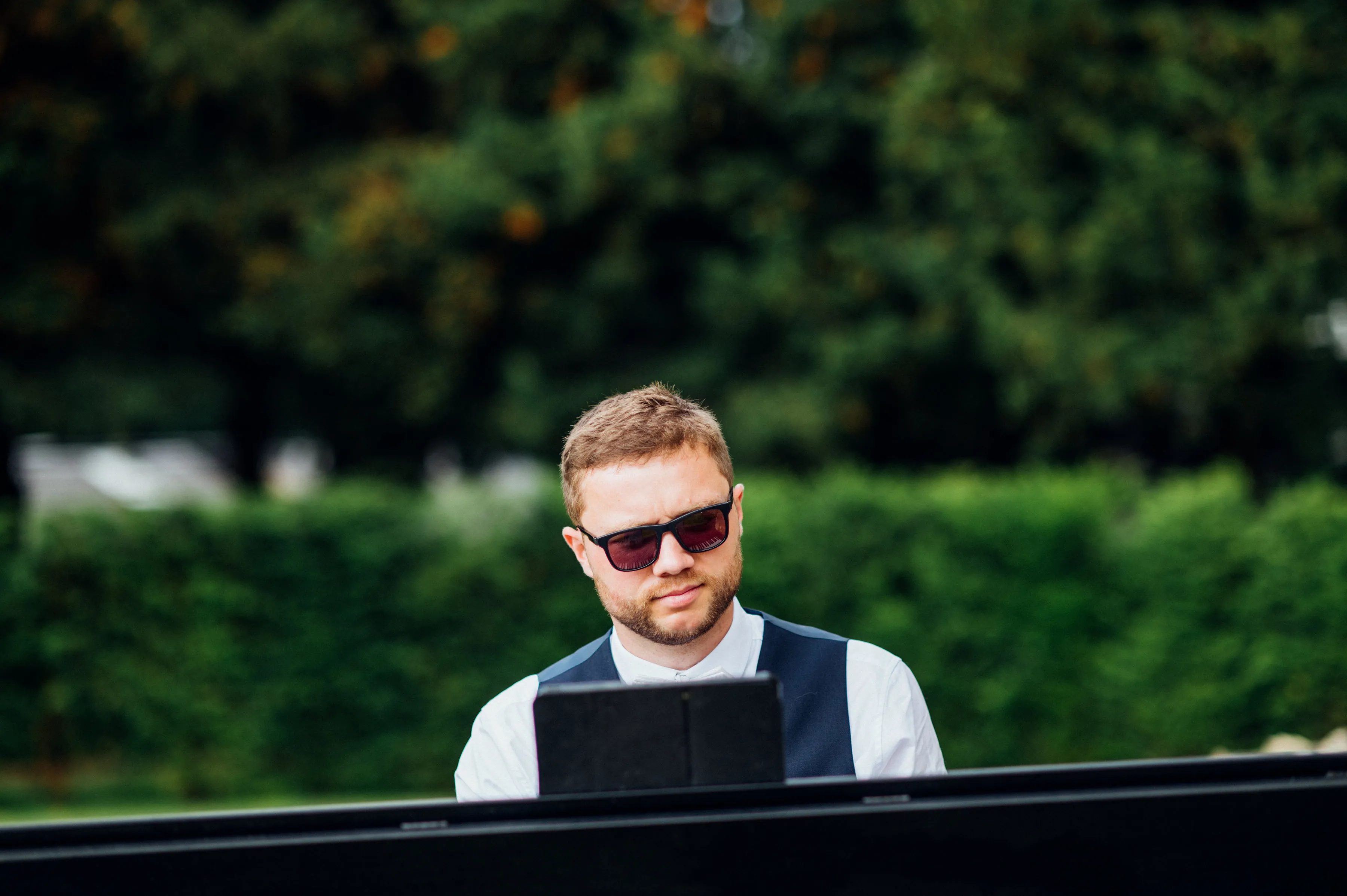 Finn Barnaby in sunglasses and waistcoat, playing piano outdoors at a summer wedding