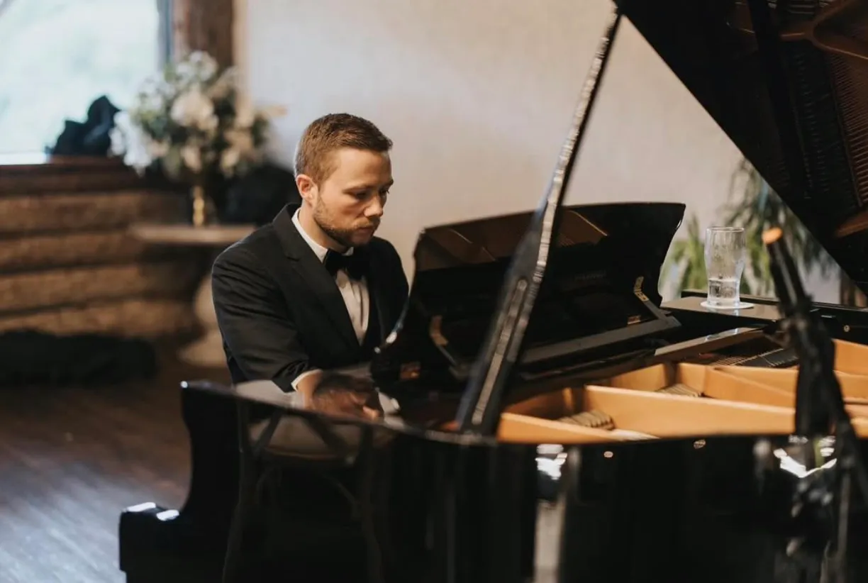 Finn in black tie playing a grand piano in a candlelit room